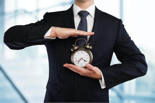 Jeune homme d'affaires en costume noir tenant une horloge sur fond