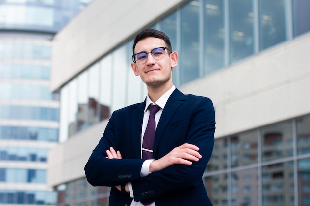 Jeune homme d'affaires en costume souriant et tenant ses mains croisées.