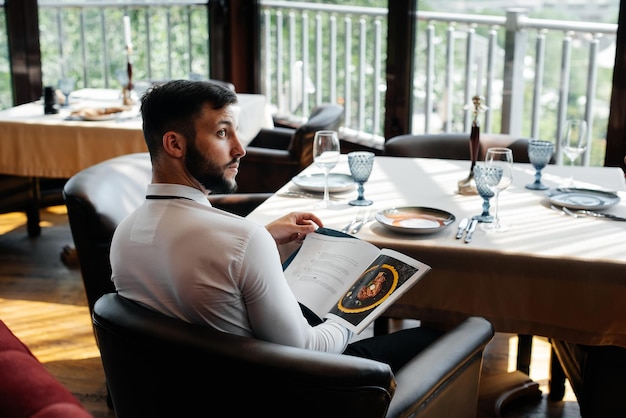 Un jeune homme d'affaires dans un restaurant raffiné examine le menu et passe une commande à un jeune serveur dans un tablier élégant Service client Service de table dans le restaurant