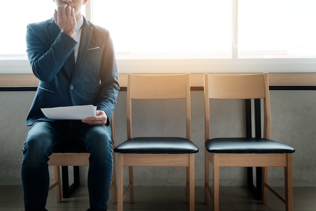 Jeune homme d&#39;affaires dans la salle d&#39;attente pour un entretien d&#39;emploi anxieux, sur une rangée de chaises.