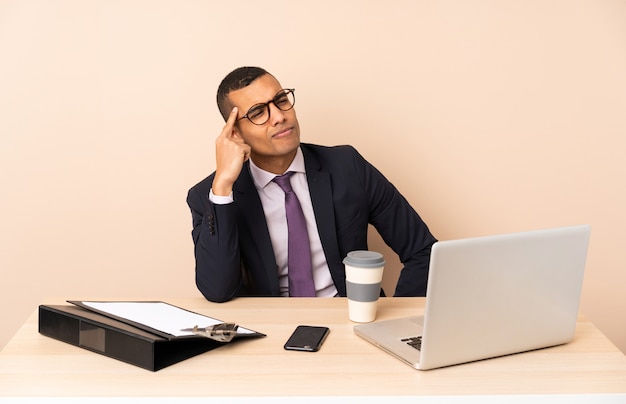 Jeune homme d'affaires dans son bureau avec un ordinateur portable et d'autres documents ayant des doutes et de la pensée