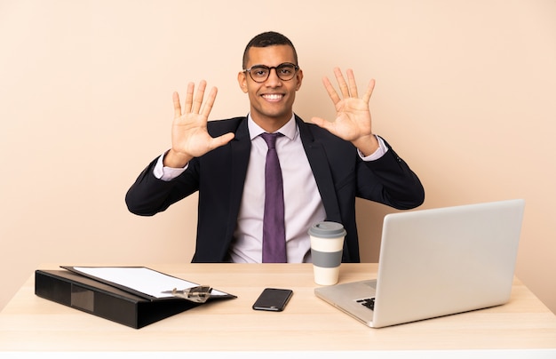 Jeune homme d'affaires dans son bureau avec un ordinateur portable et d'autres documents comptant dix avec les doigts