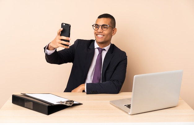 Jeune homme d'affaires dans son bureau avec un ordinateur portable et d'autres documents faisant un selfie