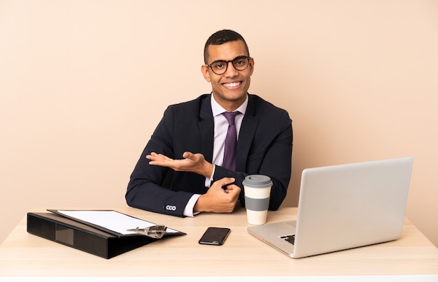 Jeune homme d'affaires dans son bureau avec un ordinateur portable et d'autres documents présentant une idée tout en regardant vers