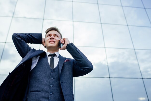 Un jeune homme d'affaires désespéré reçoit de mauvaises nouvelles de gros problèmes, parlant sur smartphone en ville à l'extérieur. debout sur fond de centre d & # 39; affaires