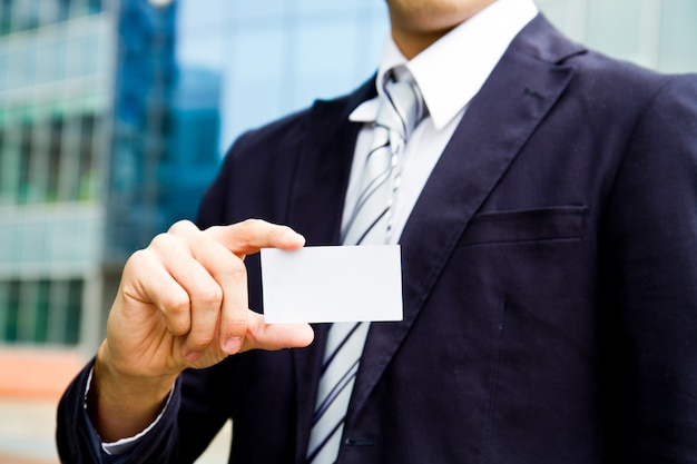 Photo jeune homme d'affaires détenant la carte de visite à la main et debout devant l'immeuble de bureaux