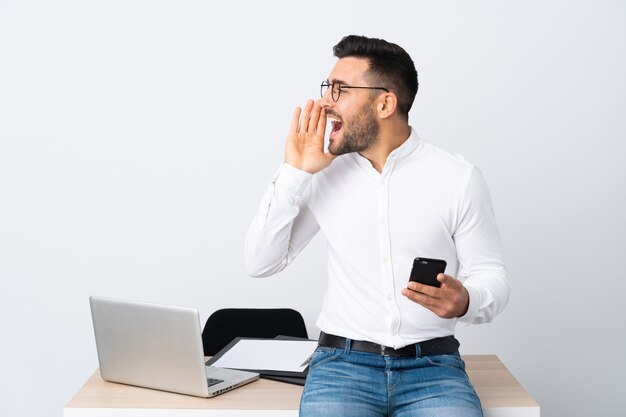 Jeune homme d'affaires détenant un téléphone mobile criant avec la bouche grande ouverte