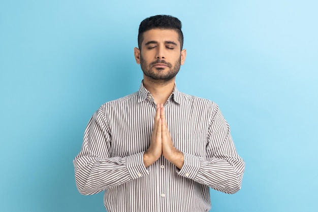 Jeune homme d'affaires détendu avec barbe debout faisant de l'exercice de méditation de yoga en gardant les paumes ensemble