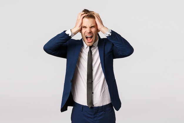 Jeune homme d'affaires en détresse a perdu tout l'argent, se sentant déprimé et déçu, fronçant les sourcils, criant de rage, se tenant la main sur la tête en difficulté, triste sur le mur blanc