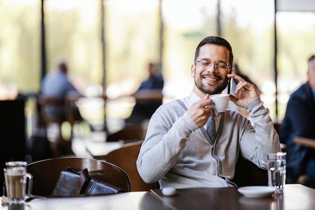 Un jeune homme d'affaires élégant boit du café à la cafétéria et a une conversation téléphonique