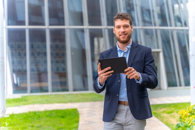 Jeune homme d'affaires ou entrepreneur à l'extérieur du bureau marchant avec une tablette à la main