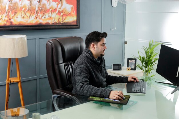 Un jeune homme d'affaires est assis au bureau et regarde un écran d'ordinateur.