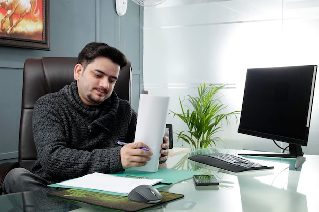 Un jeune homme d'affaires est assis au bureau et tient du papier dans les mains.