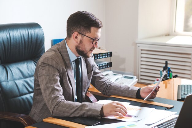 Jeune homme d'affaires étudiant des diagrammes dans son bureau personnel