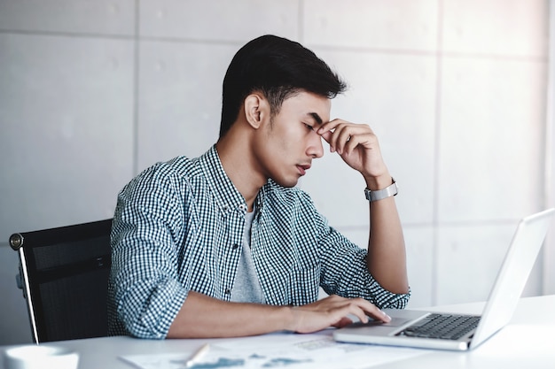 Jeune homme d&#39;affaires fatigué et stress assis sur un bureau dans un bureau avec ordinateur