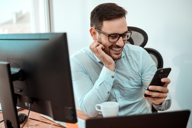 Jeune homme d&#39;affaires heureux souriant tout en lisant le message sur son smartphone.