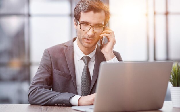 Un jeune homme d'affaires heureux en train de parler sur son smartphone à son bureau au bureau.