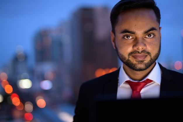 Jeune homme d'affaires indien barbu contre vue sur la ville pendant la nuit