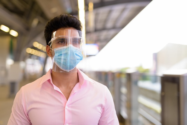 Jeune homme d'affaires indien avec masque et écran facial en attente à la gare du ciel