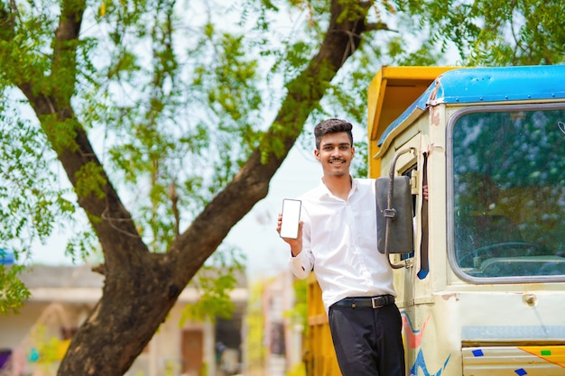 Jeune homme d'affaires indien avec son camion ou camion de fret et montrant un smartphone.