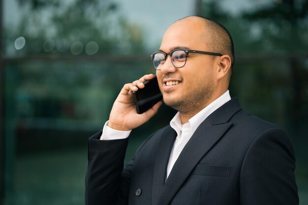 Jeune homme d'affaires indien utilisant un smartphone debout devant le bureau du bâtiment. Homme d'affaires asiatique utilisant en costume utilisant un téléphone portable.