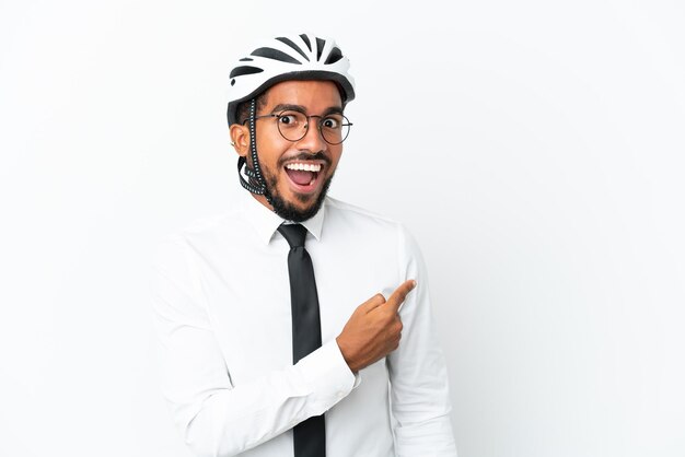 Jeune homme d'affaires latin tenant un casque de vélo isolé sur fond blanc surpris et pointant du côté