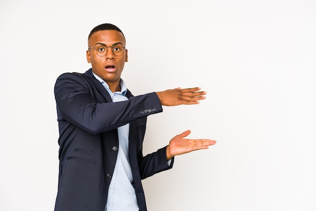 Jeune homme d'affaires latine sur mur blanc choqué et étonné tenant un espace vide entre les mains.