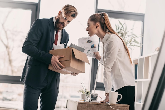 Jeune homme d'affaires licencié avec boîte en carton et femme d'affaires au bureau