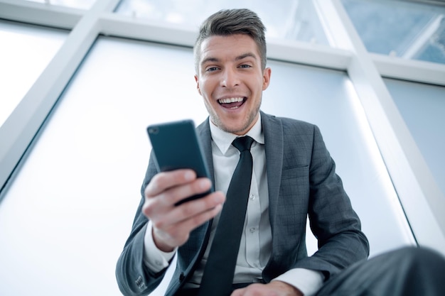 Un jeune homme d'affaires lit une bonne nouvelle dans le téléphone, il regardera dans l'appareil photo