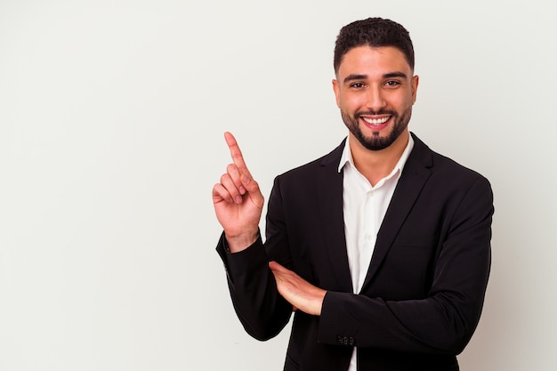 Jeune homme d'affaires métisse isolé sur blanc souriant joyeusement pointant avec l'index loin.