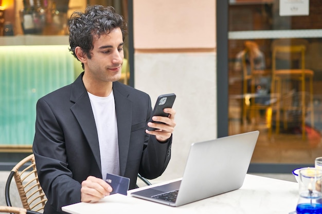 Jeune homme d'affaires multitâche avec achats en ligne dans un bar utilisant la technologie