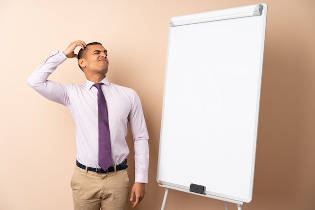 Jeune homme d'affaires sur un mur isolé donnant une présentation sur tableau blanc et ayant des doutes avec l'expression du visage confus