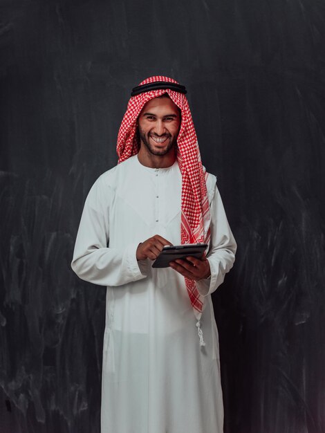 Jeune homme d'affaires musulman arabe utilisant une tablette portant des vêtements hijab devant un tableau noir.