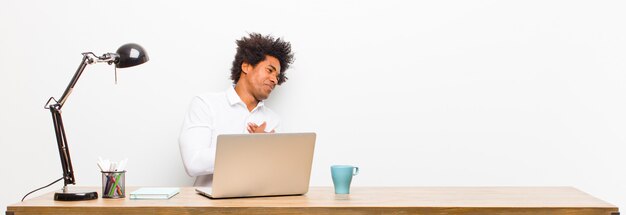 Jeune homme d'affaires noir à la recherche de triste, blessé et navré, tenant ses deux mains près du cœur, pleurant et se sentant déprimé sur un bureau