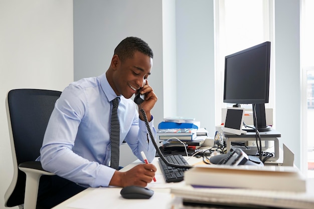 Jeune homme d'affaires noir utilisant le téléphone à son bureau