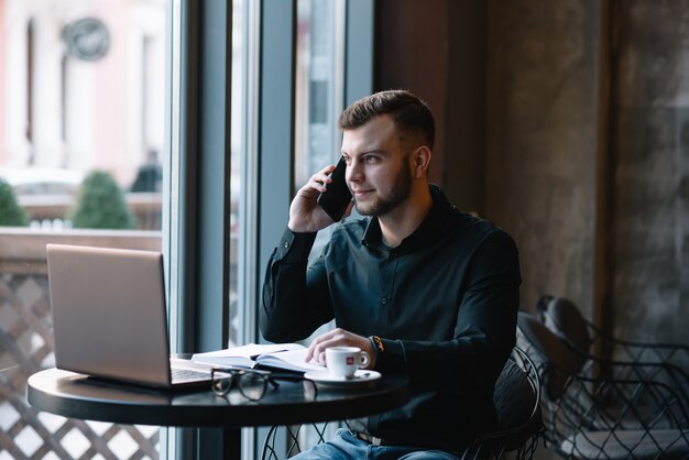 Jeune homme d'affaires parlant au téléphone mobile tout en travaillant sur un ordinateur portable au café