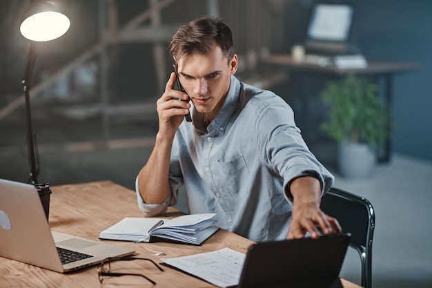 Jeune homme d'affaires parlant sur un smartphone et utilisant un ordinateur portable