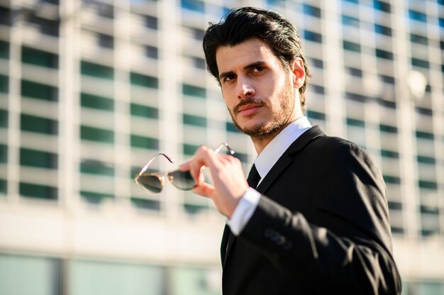 Jeune homme d'affaires en plein air tenant des lunettes de soleil