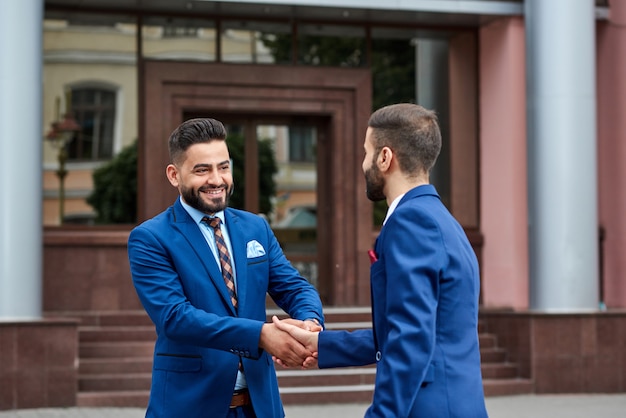 Jeune homme d'affaires poignée de main avec son partenaire commercial à l'extérieur souriant joyeusement