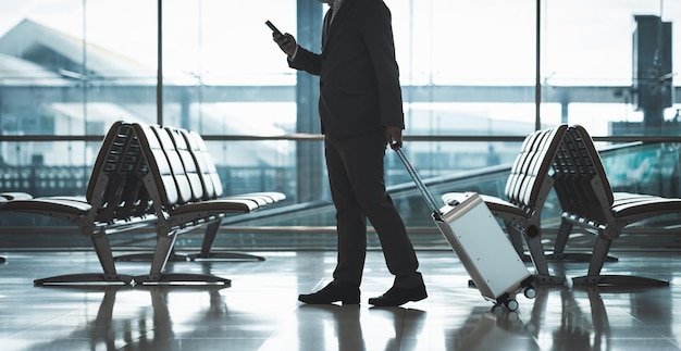 Photo jeune homme d'affaires portant un masque pour protéger le coronavirus de la grippe covid-19.il traîne les bagages en marchant dans le terminal. touriste dans le terminal de l'aéroport à l'aide d'un smartphone s'enregistrant au comptoir.