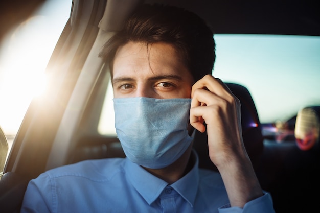 Jeune homme d'affaires prend un taxi et regarde par la fenêtre de la voiture ajustant le masque médical stérile. Concept de distance sociale.