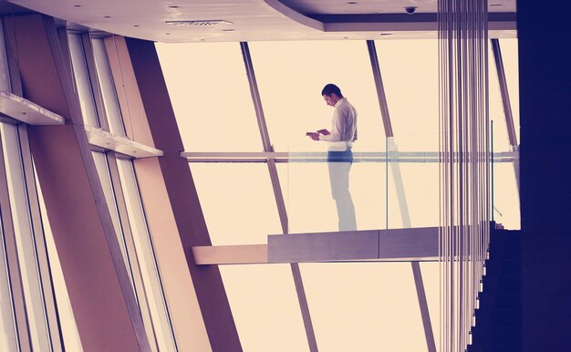 jeune homme d'affaires prospère dans un penthouse travaillant sur tbalet, intérieur d'un appartement de bureau en duplex moderne et lumineux avec escalier et grandes fenêtres