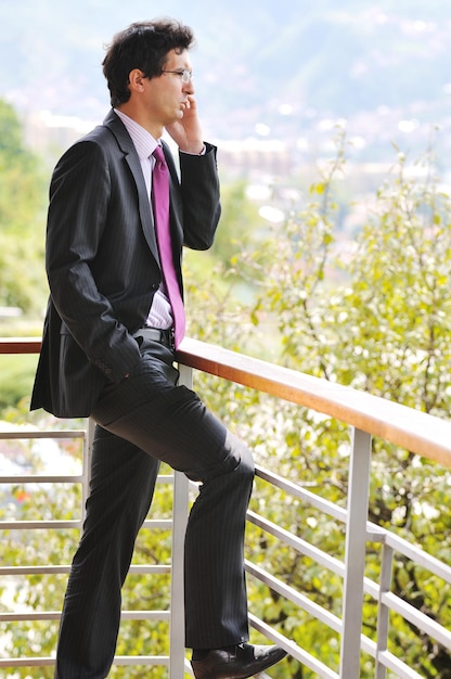 jeune homme d'affaires prospère parlant au téléphone portable en plein air sur le balcon