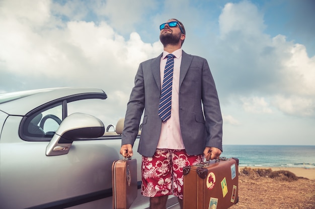 Jeune homme d'affaires prospère sur une plage Homme debout près d'une voiture classique cabriolet Vacances d'été et concept de voyage