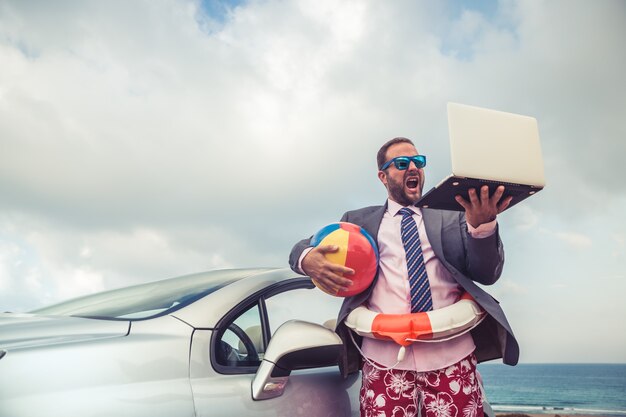 Jeune homme d'affaires prospère sur une plage Homme debout près d'une voiture classique cabriolet Vacances d'été et concept de voyage