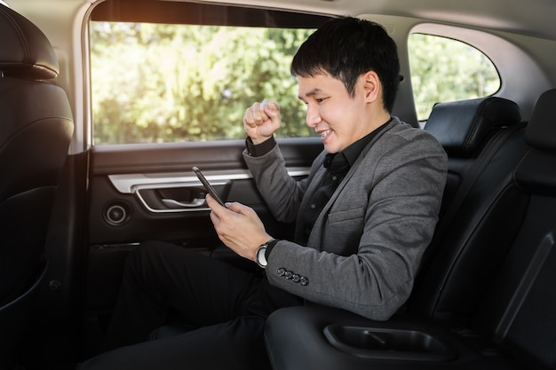 Jeune Homme D'affaires Prospère Utilisant Un Smartphone Alors Qu'il était Assis Sur Le Siège Arrière De La Voiture