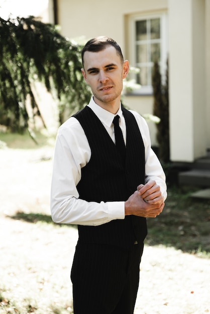 Un jeune homme d'affaires prospère vêtu de vêtements formels se dresse sur le porche de sa belle maison. les frais du marié à la maison. portrait d'un entrepreneur prospère