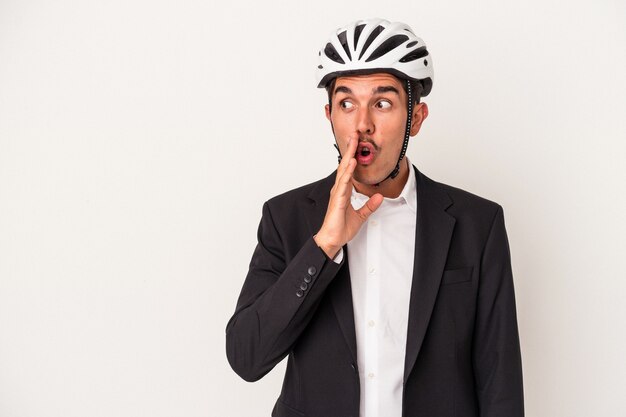 Jeune homme d'affaires de race mixte portant un casque de vélo isolé sur fond blanc dit une nouvelle secrète de freinage à chaud et regarde de côté