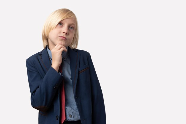 Jeune homme d'affaires réfléchi aux cheveux blonds courts et à la veste bleue qui lève les yeux et pense à quelque chose alors qu'il se tient sur un fond blanc.