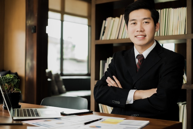 Jeune homme d&#39;affaires regarde les bras croisés intelligents et assis dans le bureau, concept d&#39;affaires